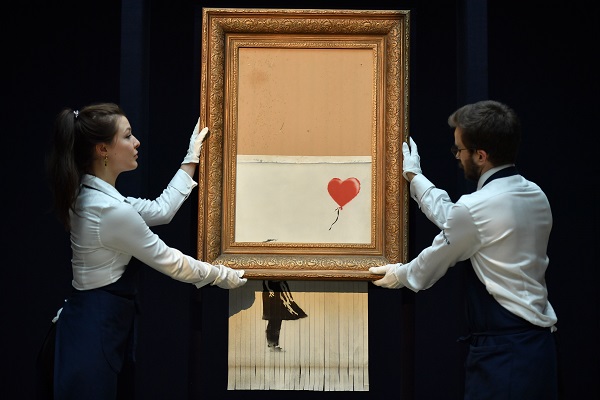 Sotheby's employees pose with the newly completed work by the artist Banksy entitled 'Love is in the Bin'